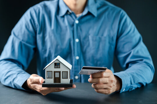 Real estate and mortgage concept. Person holding model house and credit card.