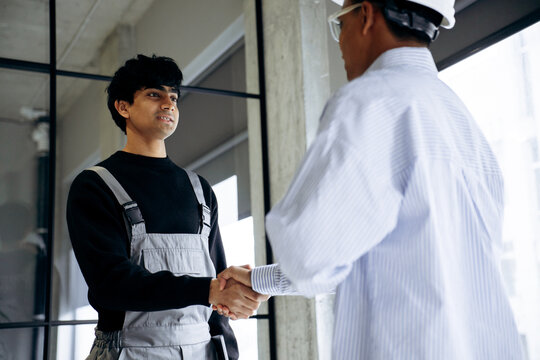 Construction worker and engineer shaking hands, finalizing a business deal on a building site. Teamwork, agreement and collaboration