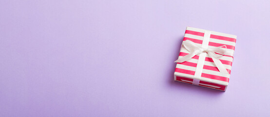 Fototapeta premium wrapped Christmas or other holiday handmade gift box in color paper with ribbon on colored background. Present box, decoration of gift on colored table, top view with copy space