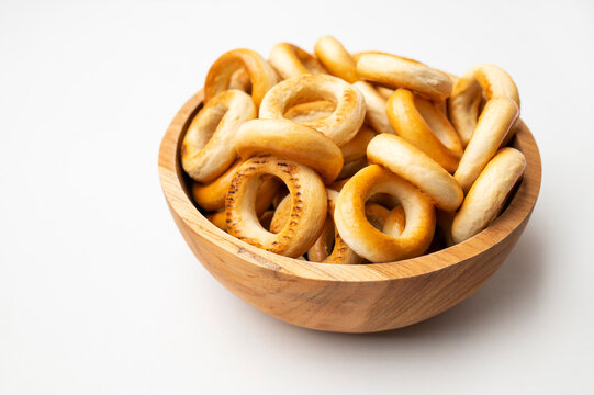 Small bagels in wooden bowl on white background, top view. Freshly baked round mini buns, dry cookies for tea, delicious flour-based pastries