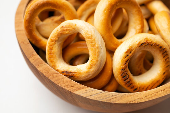 Close-up small bagels in wooden bowl on white background, top view. Freshly baked round mini buns, dry cookies for tea, delicious flour-based pastries