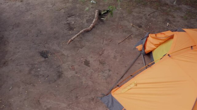 Drone flyover top view of orange tent and SUV with roof box at campsite, minimal ground textures, outdoor camping scene, travel lifestyle, road trip atmosphere, simple nature composition