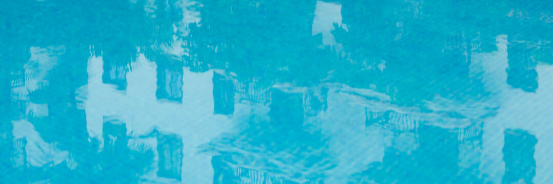 An abstract photograph of the turquoise ripples of a swimming pool, with the distorted reflection of a white building on the water's surface.