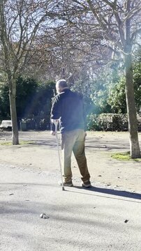 Persona con muletas mayor y convaleciente caminando lento con rodilla operada en recuperaci&oacute;n postoperatorio paso a paso con movilidad reducida en apoyo por parque y rayo de luz con reflejo
