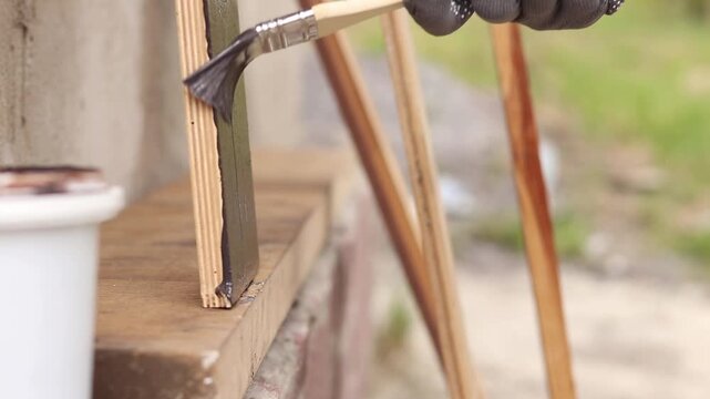Painter covers a wooden panel with brown varnish, close-up. Hand in a protective glove holds a brush, painting a wooden surface. Handmade. The process of treating wood with a protective coating