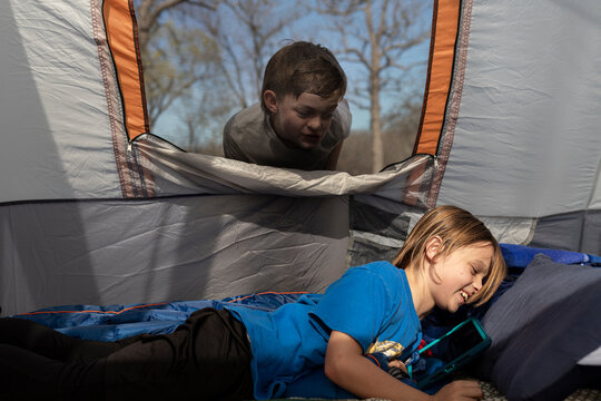 Boy smiling in a tent while another boy looks through the window
