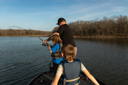 Man teaching his young son how to reel in a fishing rod from a boat