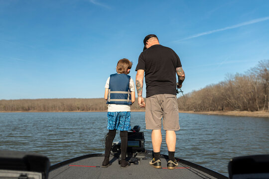 Back view of a father and son standing on boat looking at fish finder