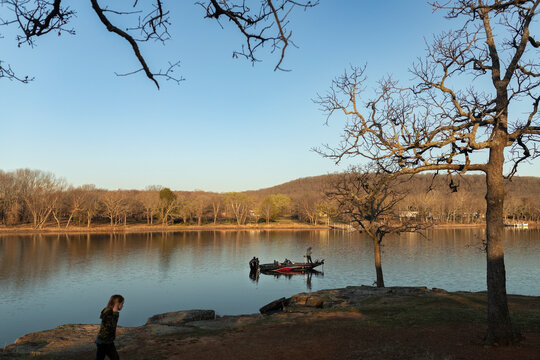 boy walking along a rocky lake bank while a man fishes in the distance