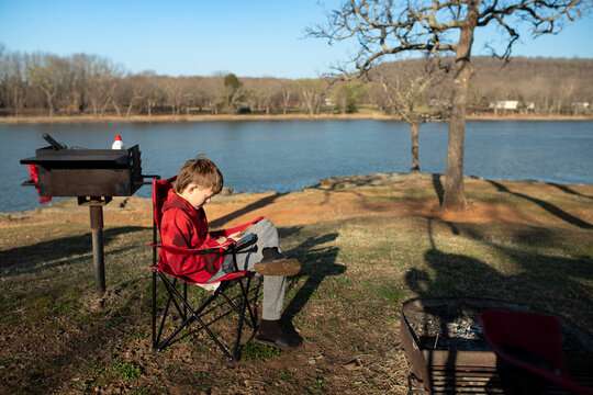 Boy sitting in a camping chair using a smartphone at a campsite