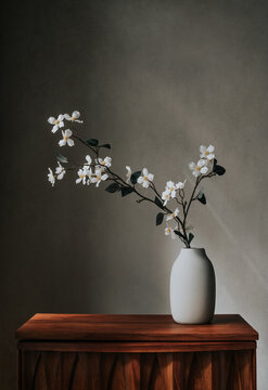 Vase with branch of white flowers on table against beige wall.