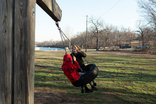 Two young boys having fun riding together on a tire swing outdoors