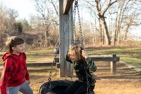 Two kids playing and interacting by a tire swing in a park setting