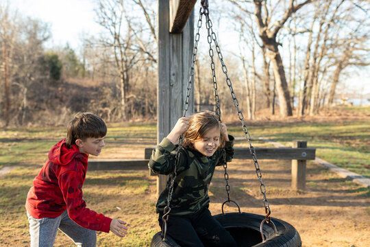 oung boy pushing his brother on a tire swing at a playground