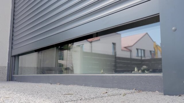 Exterior roller shutter rises over a glass window on a modern residential facade. Home security privacy smart home automation sun protection and window covering concepts