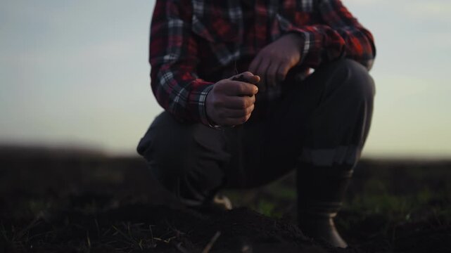 Farmer in fields, closeup view of male farm worker pouring soil on ground. Agronomist planning sowing and harvesting in farmland in ecological region, innovation and modern technology in soiling