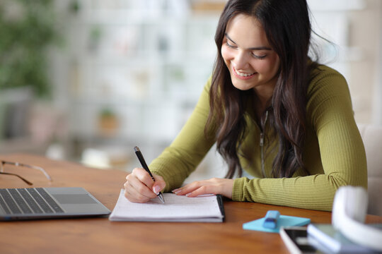 Happy student taking notes on notebook on a wooden table