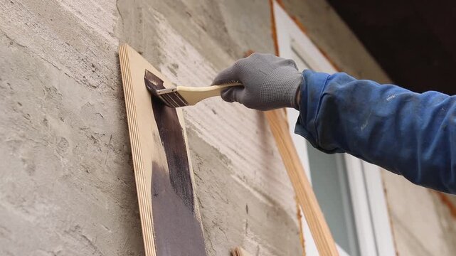 Painter covers a wooden panel with brown varnish, close-up. Hand in a protective glove holds a brush, painting a wooden surface. Handmade. The process of treating wood with a protective coating