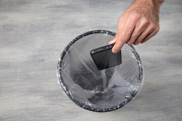 Male hand throws smartphone into the trash.