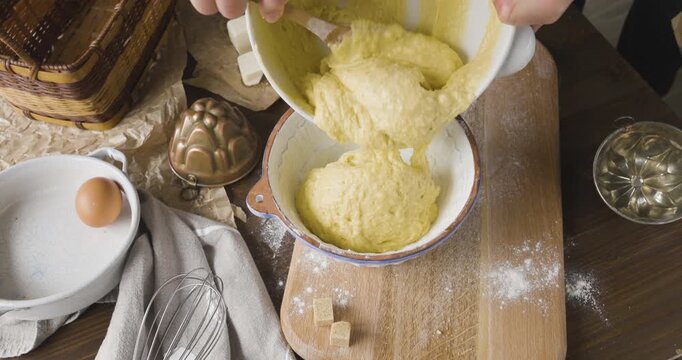 Woman hands pouring yellow cake batter from ceramic bowl into vintage baking pan. Creative kitchen hobby shows traditional dough preparation for soft and airy homemade sponge cake. 