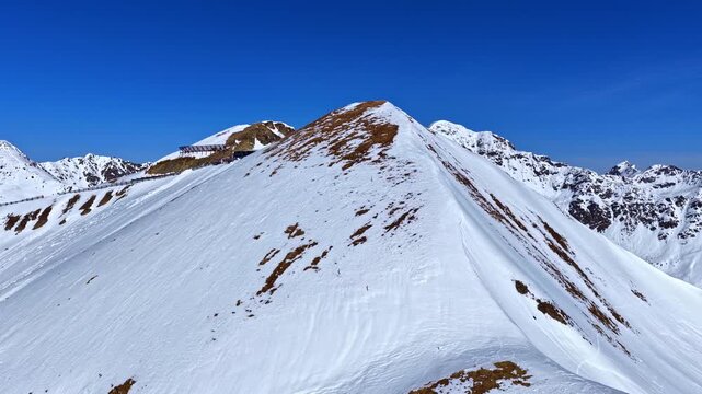 Aerial view of a ski lift mountain station on a narrow snowy ridge with skiers queuing and gondola lines. Serfaus Fiss Ladis, Austria.
