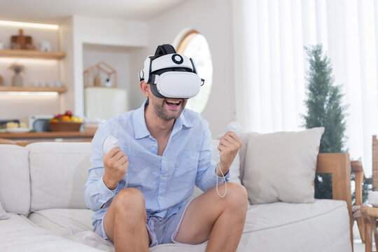 A man sits on a sofa in a living room while wearing a VR headset