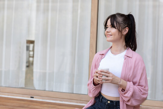 A woman enjoys her coffee while sitting cross-legged on a porch