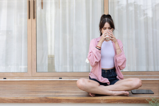 A woman enjoys her coffee while sitting cross-legged on a porch