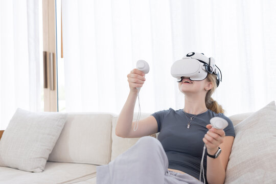Young woman enjoys virtual reality experience at home while using VR headset and controllers in a cozy living room