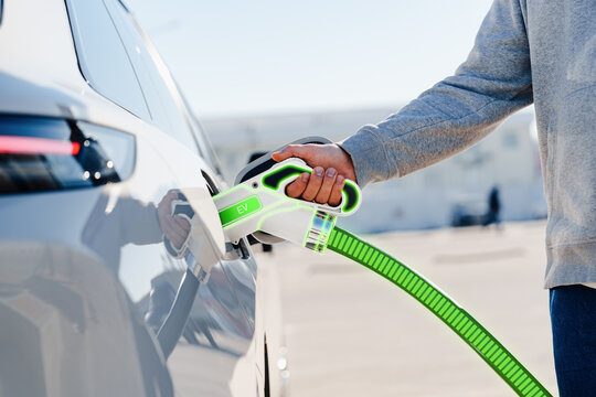 Man connects electric car to charging station for energy replenishment in parking lot
