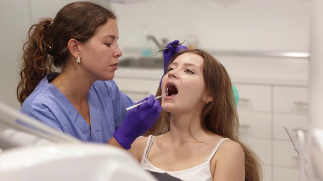 Young woman came for an examination and professional dental hygiene at a dental clinic. Woman dentist carefully examines the teeth of a client. High quality 4k footage