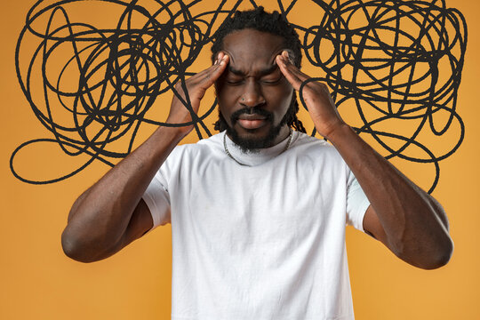 Person holds head with hands in front of orange wall while looking stressed from thoughts