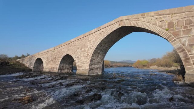 Ancient Stone Bridge over Tuzla Stream near Assos, Behramkale, Turkey Historical Ottoman Architecture and River Landscape at Sunset. High quality 4k footage