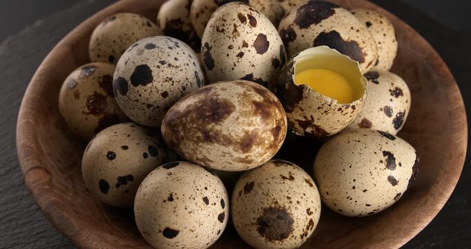 Quail eggs in a wooden bowl, close-up footage on a rotating table. Half a quail egg among a pile of whole ones.