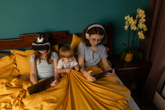 Siblings using tablet and virtual reality headset in bed