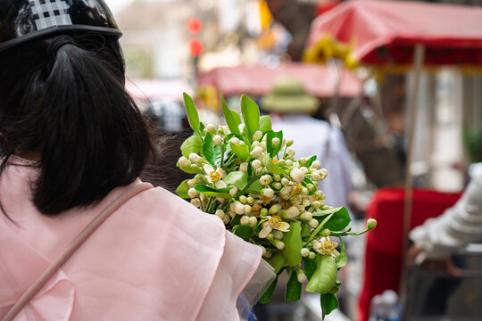 Close-up of pomelo blossom bouquet held by a woman on a bustling street with cyclo rider and soft urban background blur.