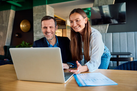 Happy businessman and businesswoman discussing over laptop in office