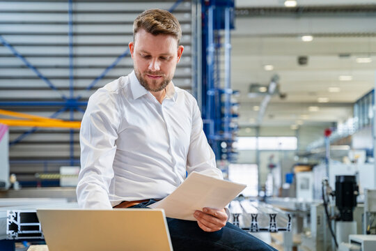 Manager checking document on laptop in production hall