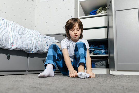 Child sitting on bedroom floor putting on a white sock