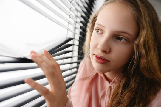 Girl looking through window blinds indoors with curiosity