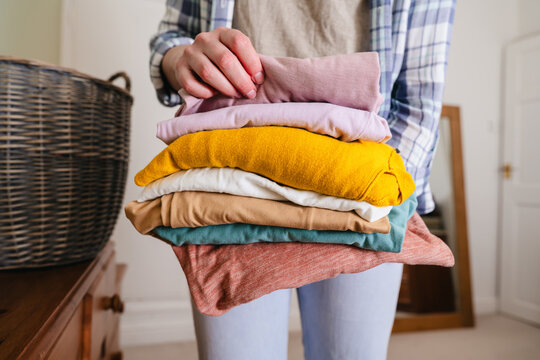 Woman holding a stack of folded colorful clothing for laundry day indoors