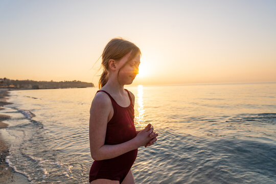 Girl standing by the sea in a swimsuit during golden hour