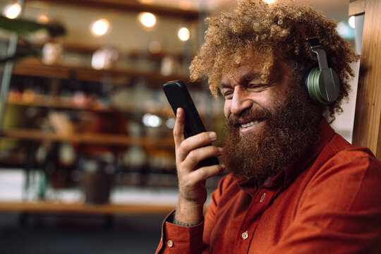 Happy businessman wearing wireless headphones listening to music and holding smart phone