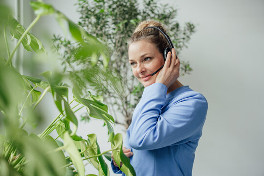 Smiling mature businesswoman talking through headset by plants in office