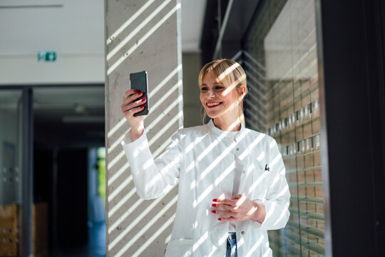 Happy blond female doctor talking on video call through mobile phone in hospital