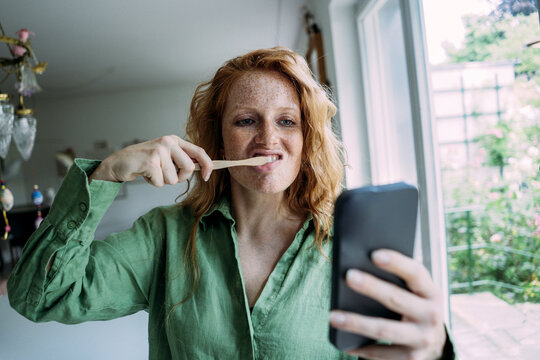 Woman using smart phone and brushing teeth at home
