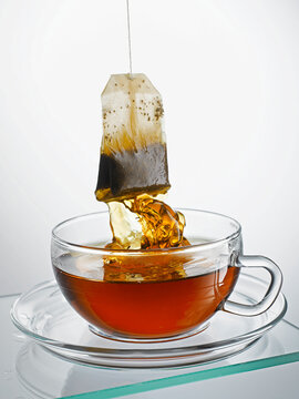 Teabag pulled from glass cup with dripping hot tea