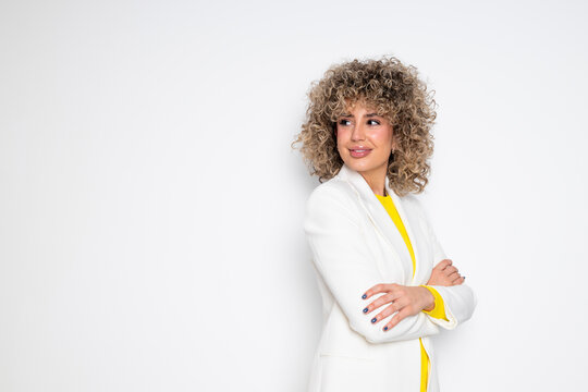 Confident business woman with curly hair in a studio wearing a white blazer and yellow sweater
