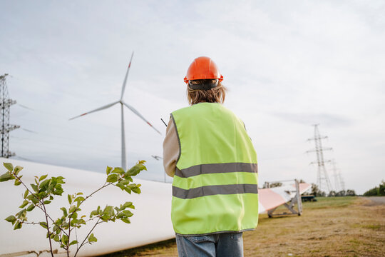 Engineer with reflective jacket standing near turbine blade at field
