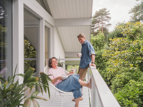 Couple relaxing and conversing on house balcony in summer